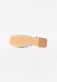 White heeled sandal with a smooth synthetic upper, square toe, and a solid tan rubber sole featuring horizontal grooves for traction.