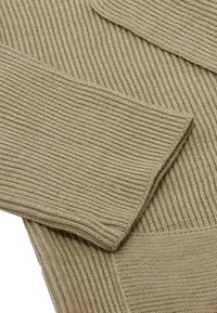 Beżowy sweter z pionowym prążkowaniem, szerokimi rękawami i kieszenią z przodu, wykonany z miękkiego materiału dzianinowego.