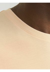 Camiseta de melocotón claro con escote redondeado y textura suave. La tela es de algodón con sutiles canalés en el collarete.