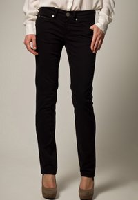 Musta slim-fit farkut, jotka on valmistettu puuvillasekoitteesta, viidellä taskulla, metalliosilla ja sileällä pinnalla. Yhdistetty vaaleansävyiseen, pitkähihaiseen paitaan.