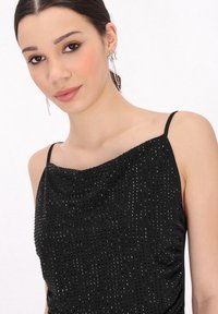 Schwarzes, mit Pailletten besetztes Top mit drapiertem Design, dünnen Trägern und glatter Textur. Verfügt über funkelnde Verzierungen im gesamten Stoff.