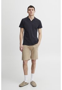 Navy polo shirt made of cotton, paired with beige shorts, white crew socks, and beige slip-on shoes. Simple design and casual style.