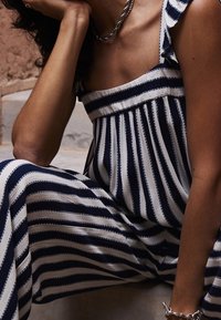 Combinaison rayée aux couleurs bleu marine et blanc, avec un décolleté droit, des bretelles à volants et une coupe ample. Tissu doux à la texture lisse.