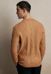 Miękki, dziany sweter w ciepłym odcieniu beżu, z teksturowanymi wzorami w diamenty i warkocze, z prążkowanym wykończeniem u dołu i na mankietach.