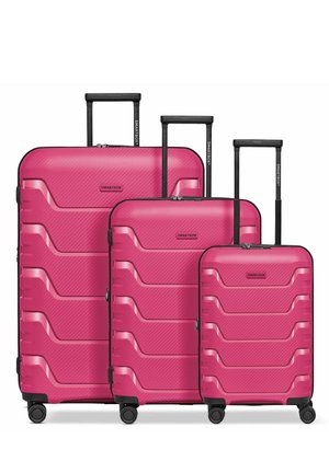 Trois valises rigides roses de tailles différentes avec des poignées télescopiques et quatre roues pivotantes chacune, disposées côte à côte.