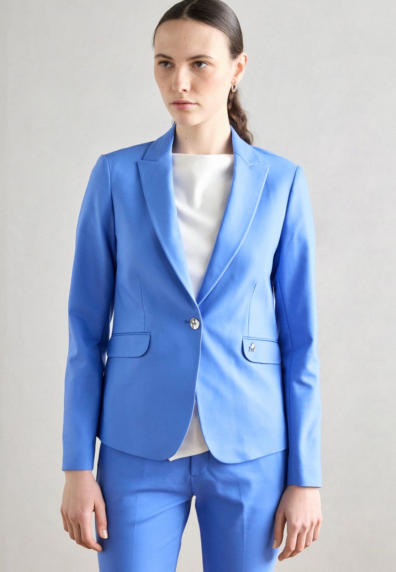 Svetle modrý přizpůsobený blazer s klopovým límcem, jednobotoným zapínáním a dvěma předními kapsami; hladká tkanina a úzký střih.
