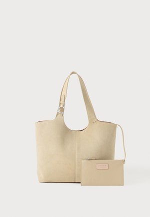 Beige suède totebag met enkele schouderriem en een bijpassend beige leren etui met rits en logo op een effen achtergrond.