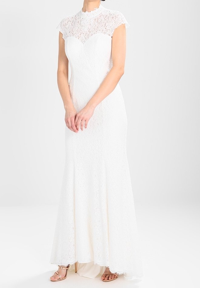 Robe de soirée en dentelle blanche avec un col montant et des manches courtes. La robe est ajustée au niveau du buste et s'évasant à partir du genou.