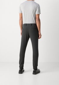 Grijs T-shirt met korte mouwen, gecombineerd met donkergrijze taps toelopende broek met twee achterzakken, gedragen met zwarte schoenen.