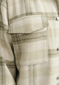 Karirani flanel košulja u krem i maslinasto zelenoj boji, s džepom na prsima, srebrnim dugmadima i mekanom teksturom.