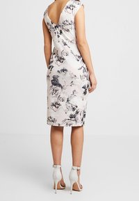 Kukkakuosisessa mekossa on istuva siluetti, vaaleanpunainen kangas, V-muotoinen kaula-aukko ja lyhyet hihat. Yhdistettynä harmaisiin nilkkaremmi-korkokengiin.