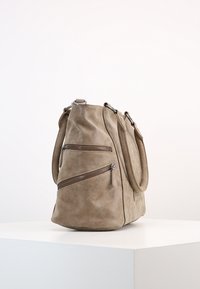 Beigefärgad mockaväska med två framfickor med dragkedja, en bred kropp och två handtag. Slät textur och mjuk silhuett med detaljer i silverfärgad metall.