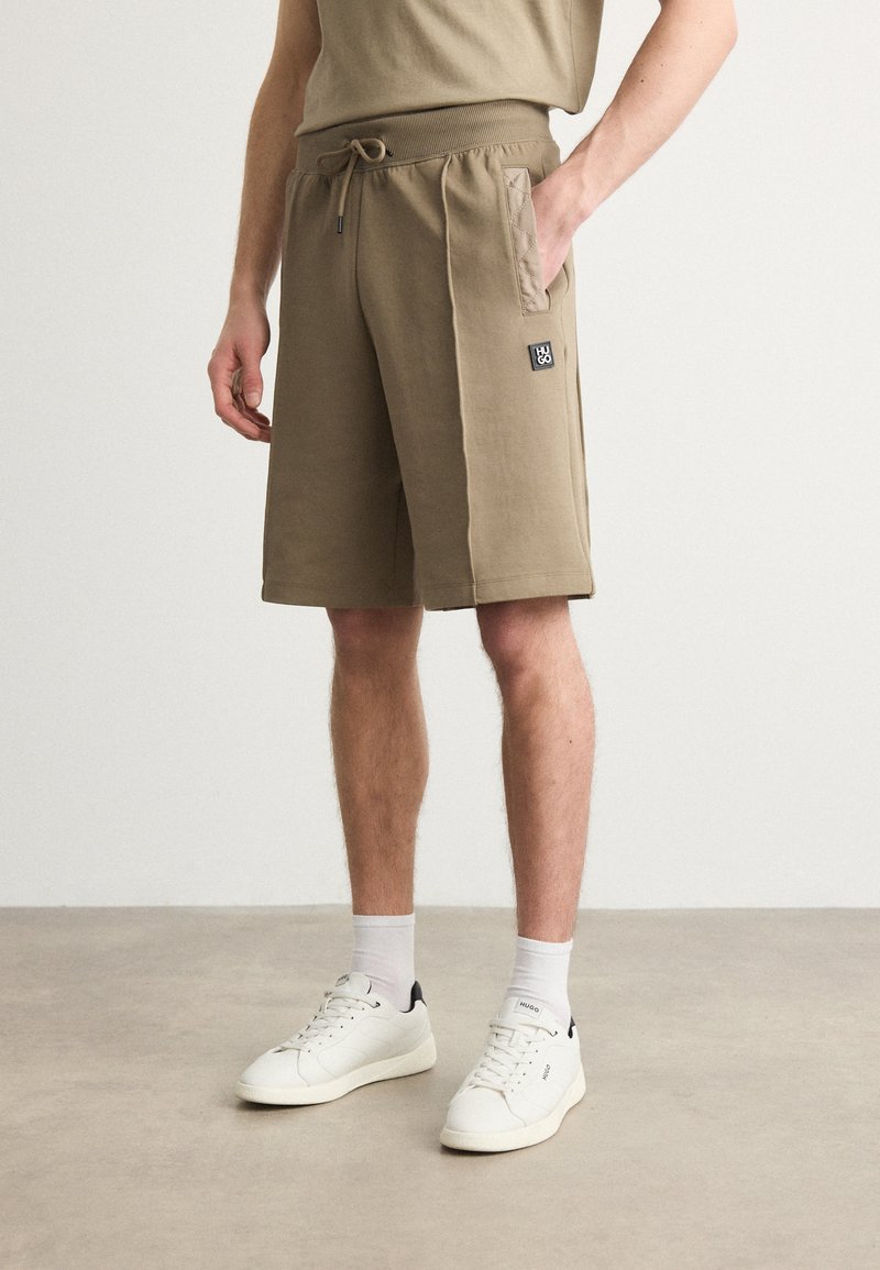 Pantaloni corti khaki con vita elasticizzata, cordino e tasche applicate. Materiale morbido con una texture liscia e dettaglio del logo del marchio.