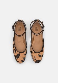 Pár plochých bot s korkovou texturou a černou květinovou výšivkou, se zapínáním kolem kotníku, označených "nae Vegan Shoes," zobrazených shora.