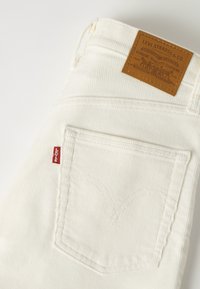 Poche blanche en velours côtelé sur un jean Levi's avec une étiquette rouge de la marque et une étiquette en cuir marron Levi Strauss & Co. au-dessus de la taille.