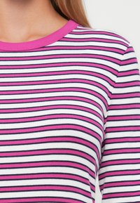 Ribbade topp med rund hals som har horisontella ränder i rosa, vitt och marinblått. Tygtexturen är slät med en kroppsnära design.