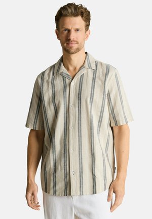 Man wearing beige short-sleeve button-up shirt with vertical gray stripes, standing against a plain light background.