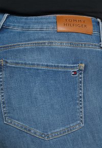 Niebieskie dżinsy z denimu z skórzaną łatą podpisaną "TOMMY HILFIGER". Charakteryzują się kontrastowym szwem i małym akcentem kolorystycznym z logo na tylnej kieszeni.