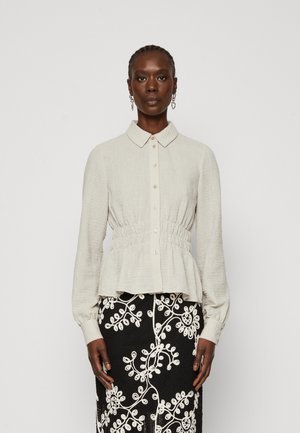 Light gray blouse with a textured finish, collared neck, button closure, and gathered waist. Paired with a black skirt featuring white floral embroidery.