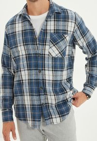 Camicia in flanella a quadri blu e bianca con taschino sul petto, chiusura con bottoni e maniche lunghe. Caratterizzata da una vestibilità comoda e una consistenza morbida.