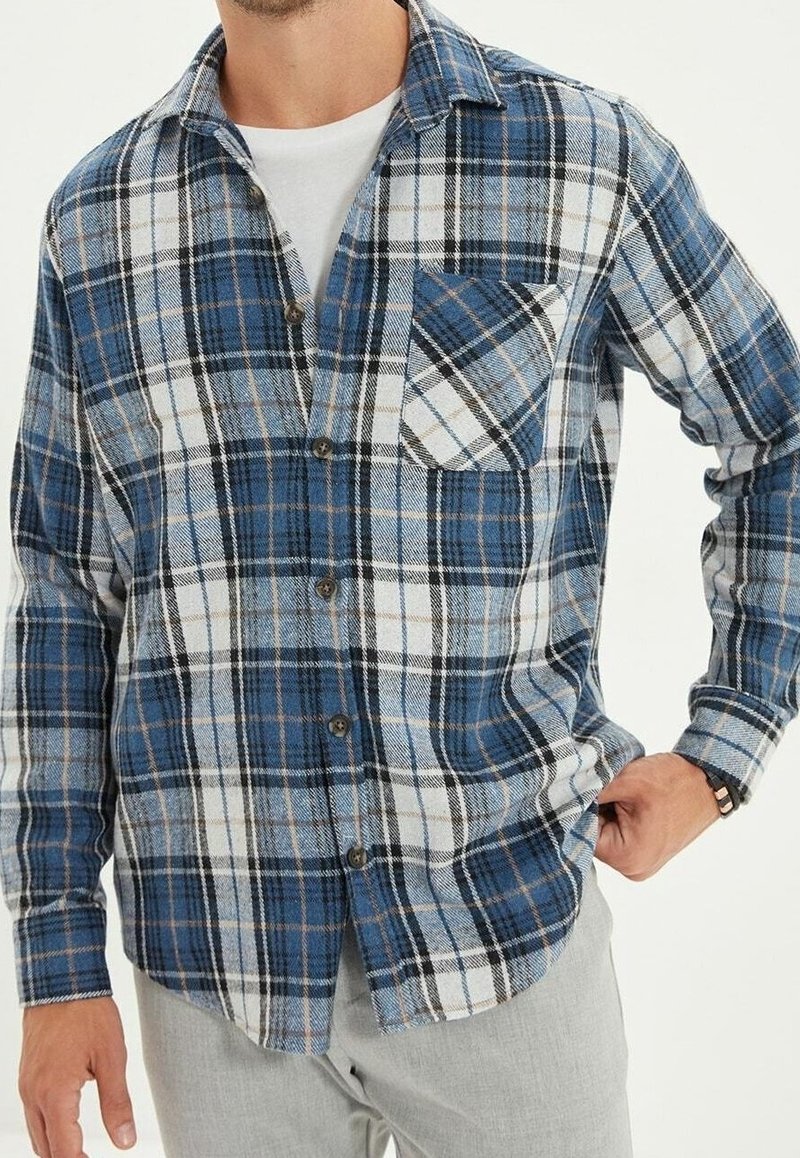 Camicia in flanella a quadri blu e bianca con taschino sul petto, chiusura con bottoni e maniche lunghe. Caratterizzata da una vestibilità comoda e una consistenza morbida.