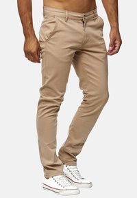 Beżowe chinosy slim-fit z zapięciem na guzik i zamek, z bocznymi kieszeniami i gładkim, bawełnianym materiałem. W zestawie z białymi trampkami.