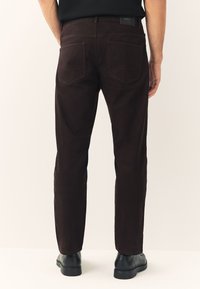 Mörkbruna byxor med rak benpassform, tillverkade av bomull. Har två bakfickor och en etikett i midjebandet. Slät textur med minimal detaljering.