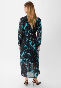 Schwarzes Kleid mit floralem Muster in Türkis. Lange Ärmel und eineTaillenschnürung. Durchscheinender Stoff mit fließender Silhouette, knielang.