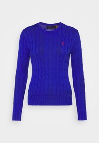 Blå stickad tröja med flätmönster, rund halsringning och ribbade muddar och fåll. Litet rött märke på vänster bröst.