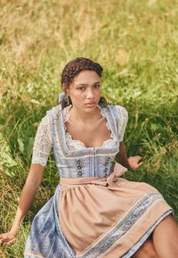 Blau-weiß gemusterter Dirndl mit Spitzenärmeln, tailliertem Oberteil und einem beigen Rock, der mit einem Satinband und dekorativen Knöpfen akzentuiert ist.