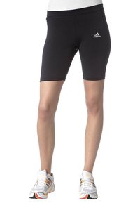 Smal passform svarta Adidas cykelshorts som bärs av en person stående, kombinerat med vita och flerfärgade träningsskor.