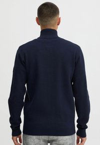 Suéter de punto azul marino con cuello alto, dobladillo y puños acanalados, y tejido texturizado. El diseño presenta un acabado suave y un corte ajustado.