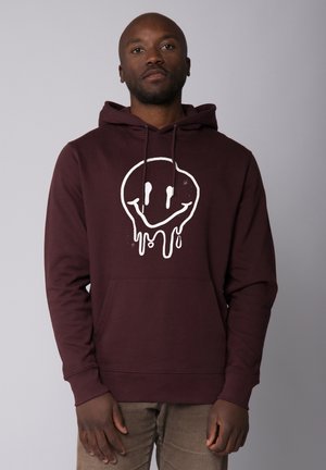 Hoodie bordeaux avec une poche avant, arborant un graphique de visage souriant gouttant en blanc. Fabriqué en tissu doux, il possède une capuche avec cordon.