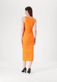Robe midi orange ajustée avec une texture froncée, sans manches et un col rond, associée à des chaussures à talons hauts noires.