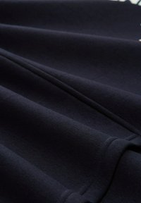 Tessuto blu navy con una superficie liscia, caratterizzato da strati piegati e cuciture visibili. Il materiale appare morbido e flessibile.