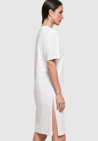 Biała bawełniana sukienka t-shirtowa, do kolan, z krótkimi rękawami, z bocznymi rozcięciami, luźny krój, prosty design, gładka tekstura.