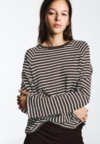 Brown and white striped long-sleeve top with a wide neckline and oversized sleeves, featuring a soft texture and relaxed fit.