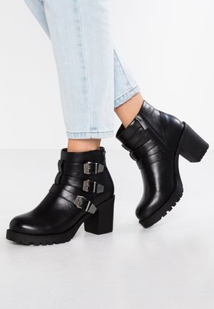 Bottines en cuir noir avec trois sangles à boucles argentées, talons massifs et semelles texturées, dotées d'une fermeture éclair sur le côté.