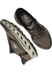 Chaussures Skechers à enfiler, présentant un dessus en maille brune légère, des accents noirs et une semelle rembourrée avec des trous de ventilation pour la respirabilité.