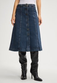 Gonna A-line in denim scuro con chiusura frontale a bottoni, passanti per cintura con fibbia circolare e dettagli di cucitura in contrasto.