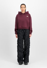 Tumepruuni lühikese varrukaga kapuutsiga kootud jakk, millel on eesmine tasku ja kuldne logo. Laiad mustad kudumispüksid tekstuuriga kangast ja stringiga vöökohaga. Mustad platvormkingad.