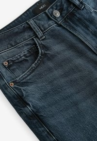 Jean en denim bleu foncé avec un design classique à cinq poches, des coutures contrastantes, une fermeture à bouton et une étiquette au niveau de la taille.