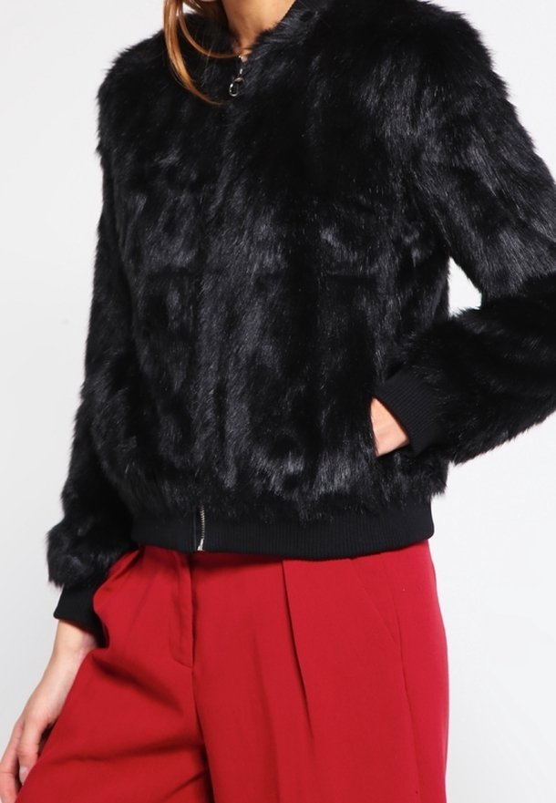 Svart fuskpäls bomberjacka med dragkedja framtill, ribbade ärmslut och nederkant. Har en rundad halslinning och sidofickor.