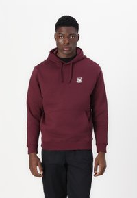 Hoodie bordeaux avec une poche avant, capuche à cordon de serrage, et petit logo blanc sur la poitrine gauche. Tissu doux et poignets côtelés.