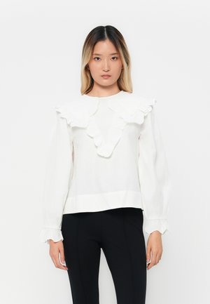 Hvit bluse med volangkrage og mansjetter, lange ermer og løs passform. Har teksturert stoff og et enkelt, minimalistisk design.