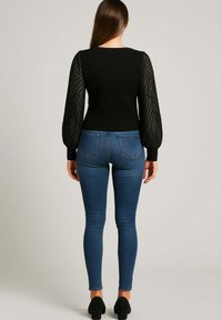 Top nero a coste con maniche a sbuffo trasparenti e testurizzate, abbinato a jeans skinny blu scuro e tacchi neri, che mette in risalto una silhouette aderente.