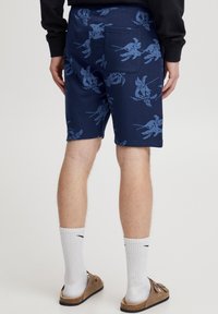 Temno modri kratki hlači z nežnim svetlo modrim cvetličnim vzorcem, izdelani iz mehke tkanine. Vključujejo zadnji žep in sproščen kroj.