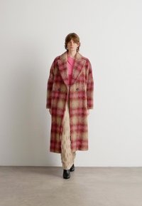 Lange geruite jas in rood en beige, gemaakt van een zachte, textuurstof, met een dubbelzijdige voorkant en brede revers, gedragen over een roze top.