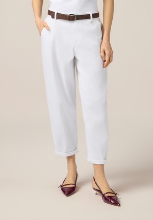 Pantalons blancs amples avec des ourlets retroussés, assortis à une ceinture en cuir marron. Talons slingback en cuir verni bordeaux avec des pointes effilées.
