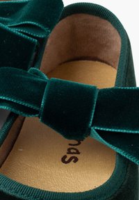 Zielone płaskie buty z weluru z dużą kokardą z przodu, miękkim wnętrzem i teksturowaną podeszwą; zaprojektowane z myślą o komforcie i stylu.